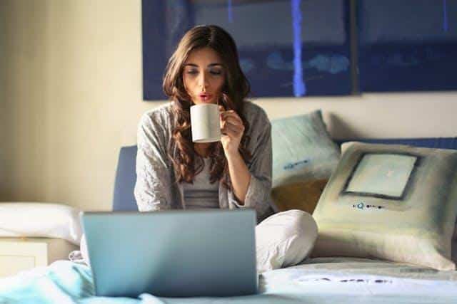 A woman drinking from a mug and using her laptop